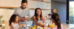Familia feliz disfrutando de desayunos saludables con frutas, jugos y cereales en la cocina de su hogar